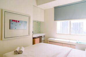 Quarto de hotel com cama, pequena escrivaninha, espelho e janela com vista para edifícios.