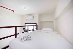 Een hotelkamer met een enkel bed, wit beddengoed, een houten hoofdbord, een wandairconditioner en een plafondlamp.