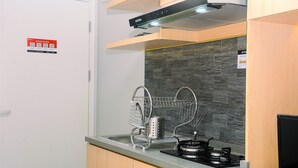 A modern kitchen with a built-in stove, a dish rack, and a stone backsplash. - Fully Furnished Studio At Springlake Summarecon Apartment (Bekasi)