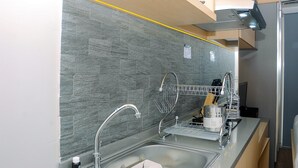 A modern kitchen with a grey stone backsplash, stainless steel sink, and a dish drying rack. - Fully Furnished Studio At Springlake Summarecon Apartment (Bekasi)