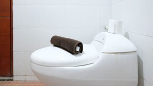 Eine weiße Toilette mit einem braunen Handtuch auf dem Deckel und einem Toilettenpapierhalter an der Wand.