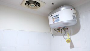 Ein Badezimmer mit weiß gefliesten Wänden, einem Deckenventilator und einem an der Wand montierten Warmwasserbereiter.