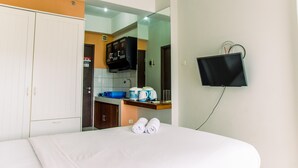 A hotel room with a bed, a TV mounted on the wall, a kitchen area with a microwave, and a wardrobe. - Cozy Stay Studio Apartment At Easton Park (South Tangerang)