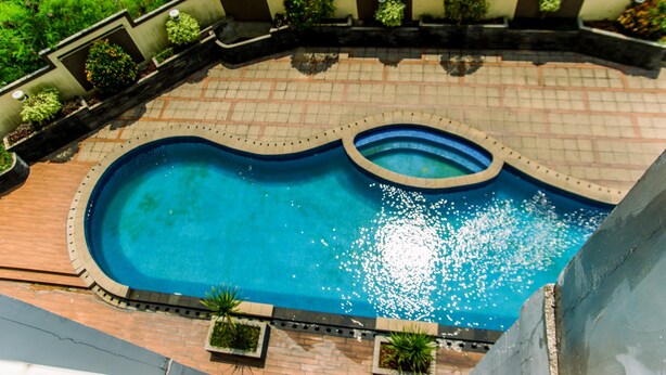 A swimming pool with a curved design, surrounded by a brick patio and bordered by planters with greenery. - Cozy Stay Studio Apartment At Easton Park (South Tangerang)