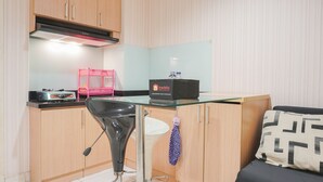 A compact kitchen with wooden cabinets, a glass countertop, a black chair, and a small table. - Comfort Living 1Br At The Boulevard Apartment (Jakarta)
