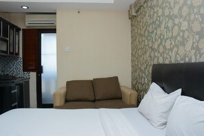 A hotel room with a bed, a sofa, a small kitchenette, and a patterned wallpaper. - Minimalist Studio Room At Kebagusan City Apartment (Jakarta)