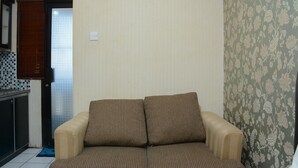 A living room with a beige sofa, a patterned wallpaper, and a tiled floor. - Minimalist Studio Room At Kebagusan City Apartment (Jakarta)