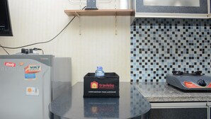 A kitchen with a refrigerator, a microwave, a sink, and a stove. There is a small shelf above the sink with a kettle and a bottle of water. The wall has a tiled backsplash. - Minimalist Studio Room At Kebagusan City Apartment (Jakarta)