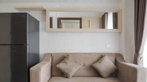 A living room with a beige sofa, two cushions, a black refrigerator, and a mirror above the sofa. - Comfort And Warm 2Br At Parkland Avenue Apartment (South Tangerang)