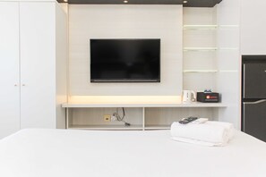 A modern hotel room with a flat-screen TV mounted on the wall, a bedside table with a remote control, a power strip, and a travel adapter. - Fancy And Nice Studio @ Springlake Summarecon Bekasi Apartment (Bekasi)
