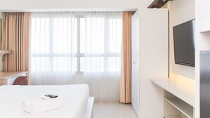 A hotel room with a bed, a TV mounted on the wall, and a window with curtains. - Fancy And Nice Studio @ Springlake Summarecon Bekasi Apartment (Bekasi)