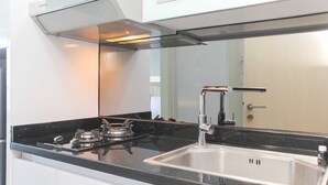 A modern kitchen with a gas stove, stainless steel sink, and white cabinetry. - Fancy And Nice Studio @ Springlake Summarecon Bekasi Apartment (Bekasi)