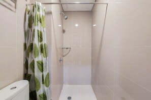 A small, enclosed shower area with a toilet to the left, tiled walls, and a shower curtain with a leaf pattern. - Comfort And Elegant Studio Apartment At B Residence (Pagedangan)