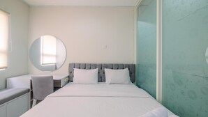 Een slaapkamer met een bed, een bureau, een stoel en een ronde spiegel.