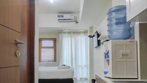 Une chambre d’hôtel équipée d’un lit, d’une petite kitchenette, d’un distributeur d’eau et d’un ventilateur de plafond.