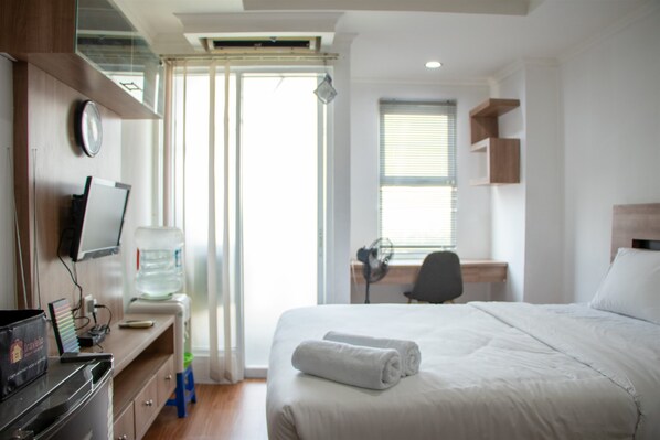Relax in a serene space with a neatly made bed, desk, and flat-screen TV.
