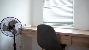 A workspace with a desk, chair, and standing fan. - Nice And Comfort Studio Apartment At Belmont Residence Puri (Jakarta)