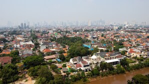 A densely populated urban area with a mix of residential and commercial buildings, a river running through the scene, and a distant city skyline. - Nice And Comfort Studio Apartment At Belmont Residence Puri (Jakarta)