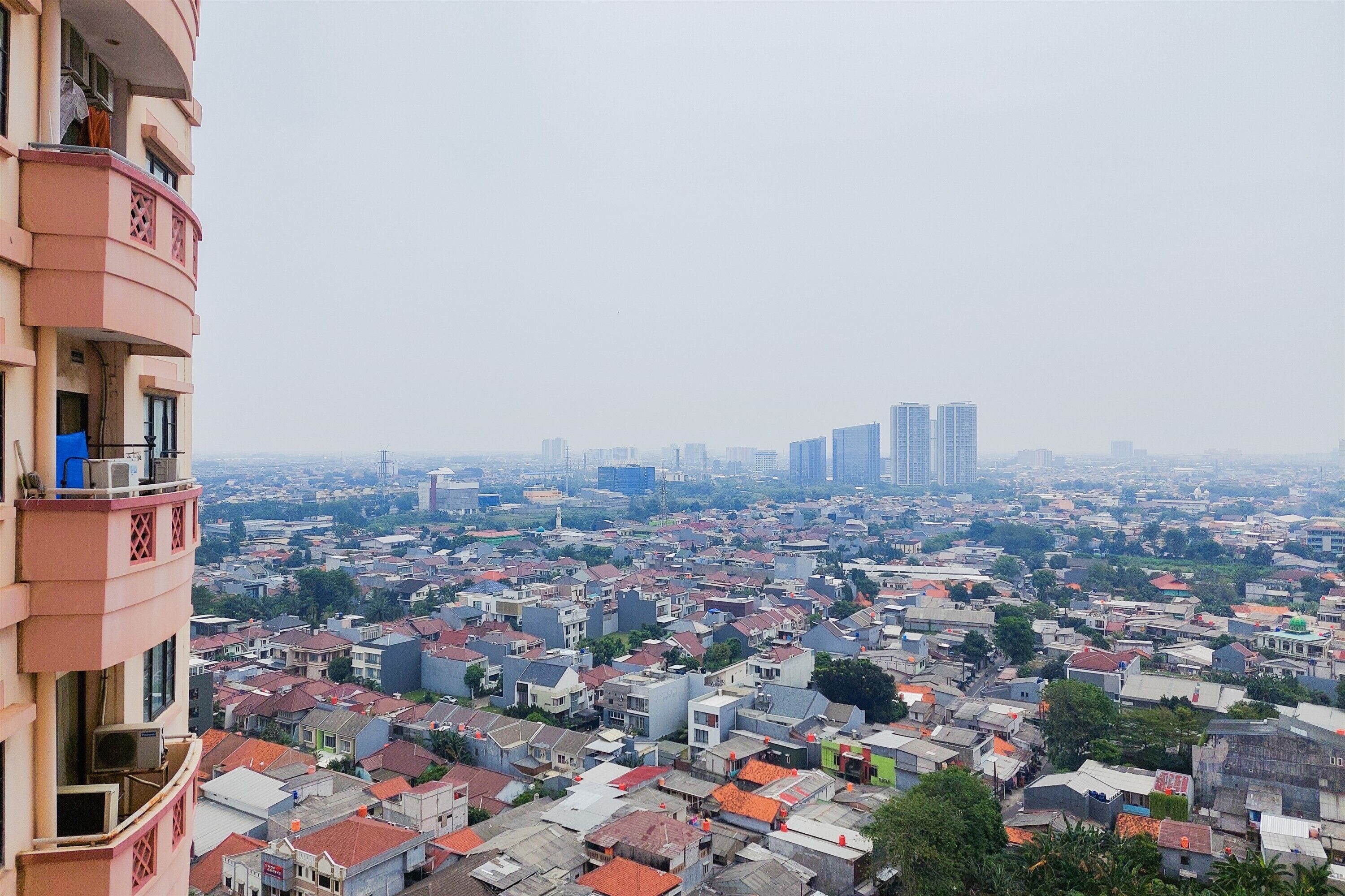 A high-rise building with multiple balconies overlooking a densely populated urban area with a mix of residential and commercial buildings.