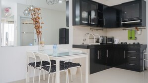 A modern kitchen with black cabinets, a glass dining table, and white chairs. - Strategic And Homey 2Br At Puri Garden Apartment Near Mall (Jakarta)