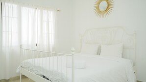 A white bedroom with a bed, curtains, and a sunburst mirror on the wall. - Strategic And Homey 2Br At Puri Garden Apartment Near Mall (Jakarta)