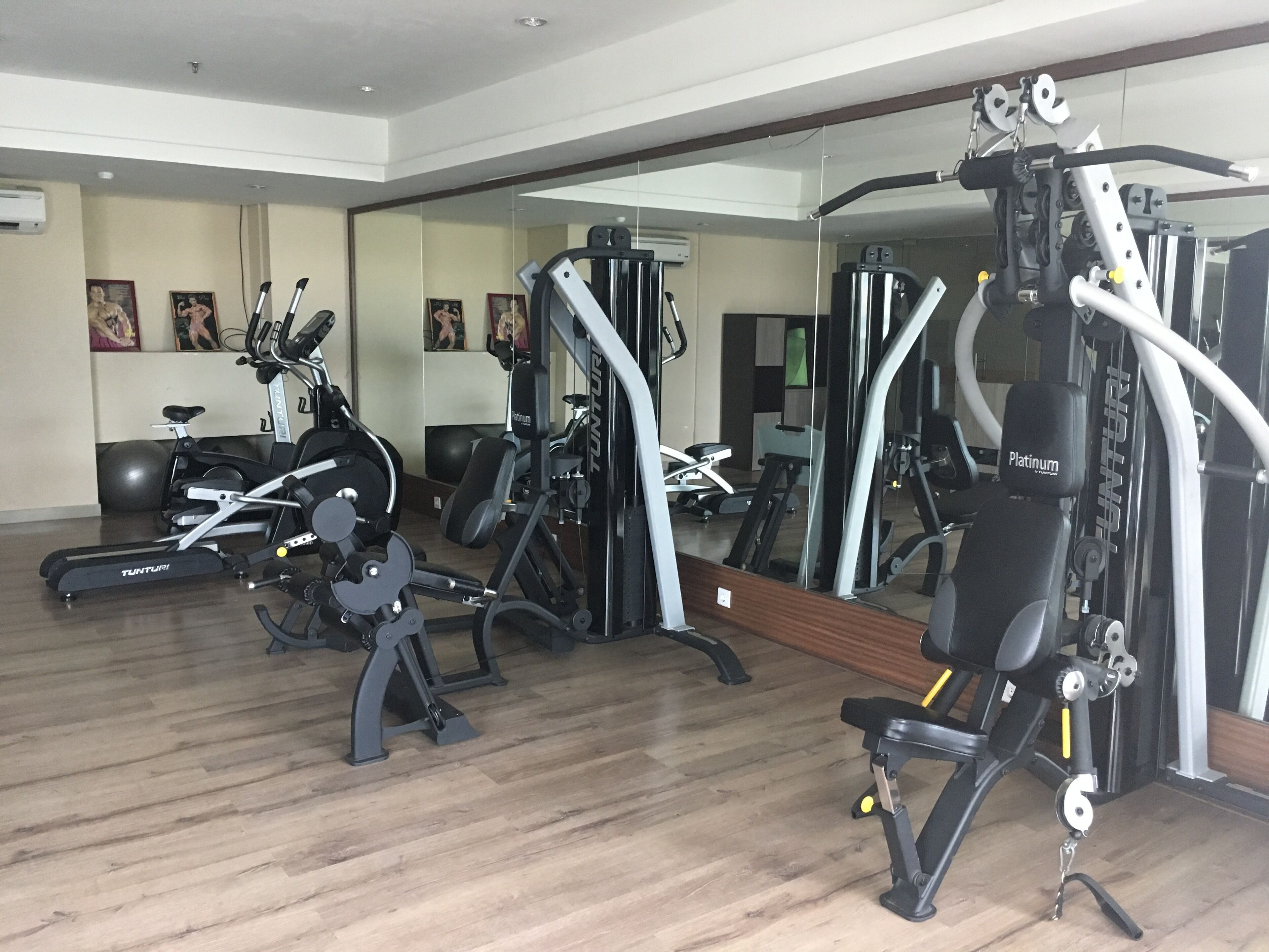 Een fitnessruimte met diverse fitnessapparaten, waaronder loopbanden, krachttrainingsmachines en een spiegelwand.