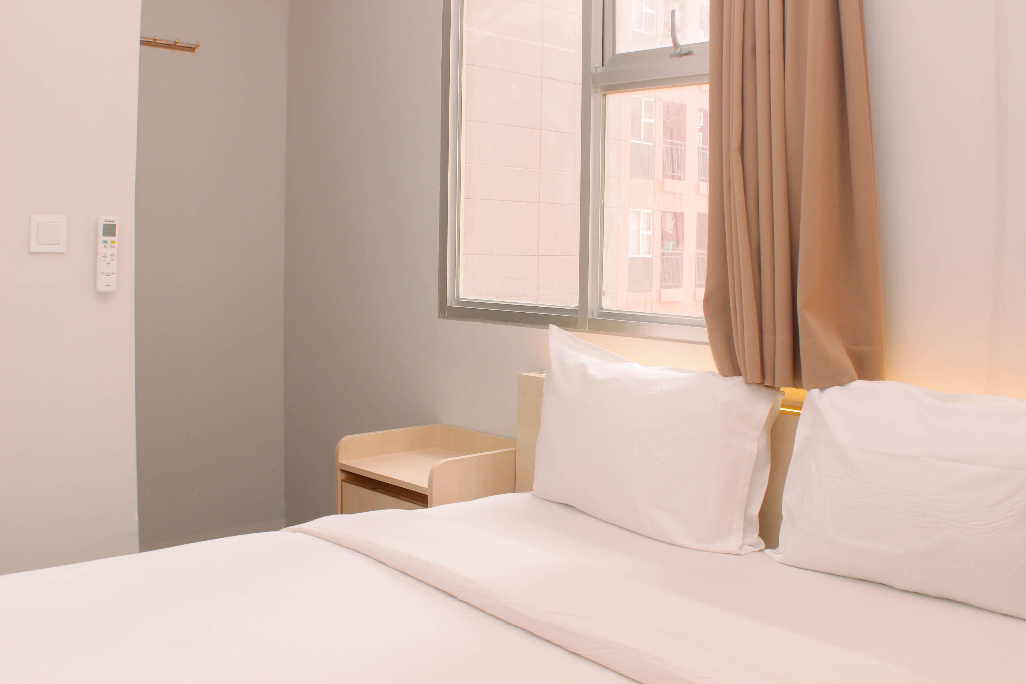 Ein ordentlich bezogenes Bett mit weißen Laken, ein Nachttisch und ein Fenster mit Vorhang.