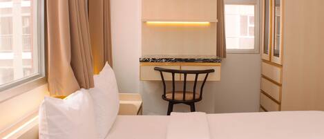A hotel room with a bed, a chair, a desk with a mirror, and a window with curtains.