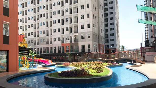 Piscina com uma ponte, rodeada por vegetação e um parquinho.
