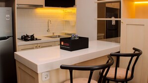 Cozinha compacta com armários brancos, bancada, pia, fogão e uma caixa preta com garrafas. Duas cadeiras estão na bancada.