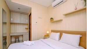 A hotel room with a bed, a desk, a chair, a nightstand, and a wall-mounted shelf. - 1Br Apartment With Cozy Design At Royal Olive Residence (Jakarta)