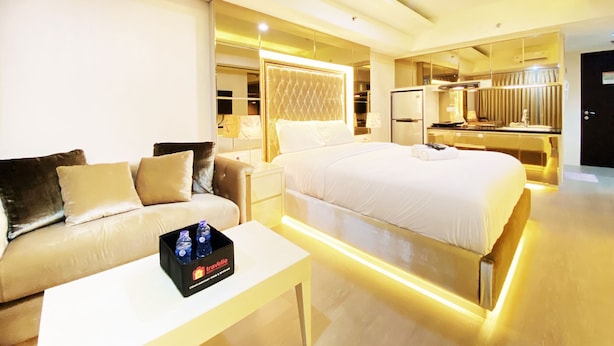 A modern hotel room with a large bed, a sofa, a small table with a bottle of water, and a minibar. - Cozy Studio Room At Tamansari La Grande Apartment (Bandung)