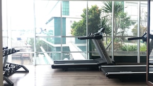 A gym with treadmills and dumbbells, large windows with a view of buildings and trees. - Cozy Studio Room At Tamansari La Grande Apartment (Bandung)