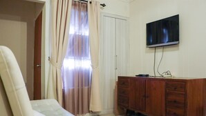 A bedroom with a bed, a wooden dresser, a television on the wall, and a door with a curtain. - Nice And Elegant 2Br At Grand Palace Kemayoran Apartment (Jakarta)