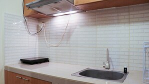 A kitchen with a white tiled backsplash, a stainless steel sink, and wooden cabinets. - Nice And Elegant 2Br At Grand Palace Kemayoran Apartment (Jakarta)