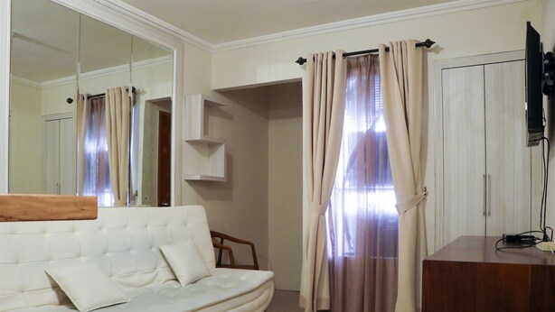 A hotel room with a white sofa, a wooden desk, a mirror, and a wardrobe. - Nice And Elegant 2Br At Grand Palace Kemayoran Apartment (Jakarta)
