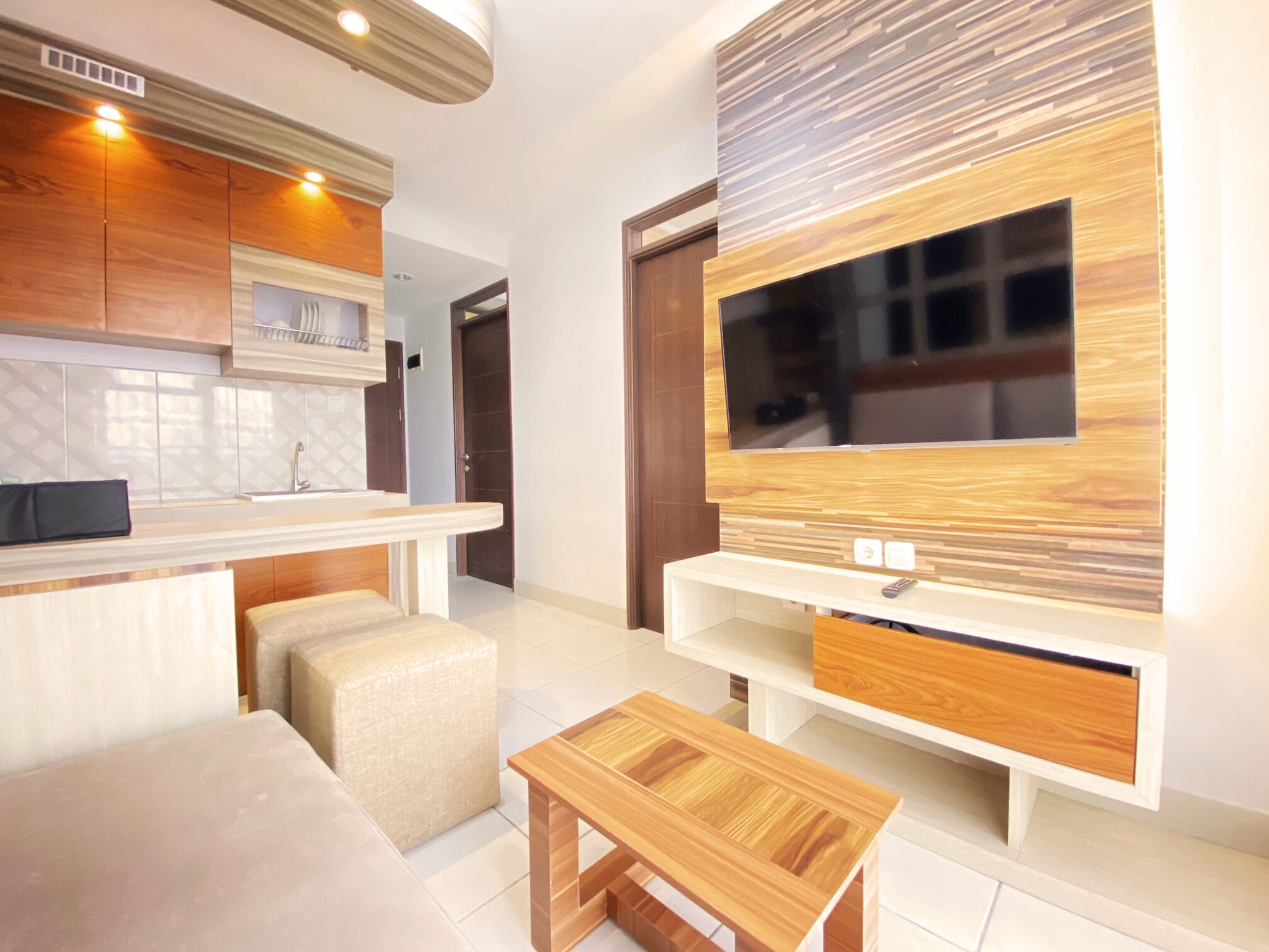A modern kitchen with wooden cabinets, a built-in oven, and a large TV mounted on the wall.