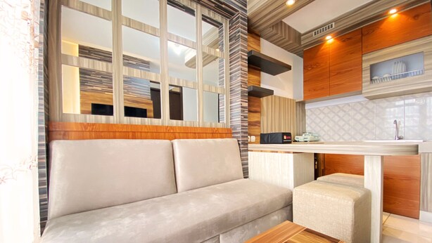 A modern living room with a sofa, a wooden coffee table, and a kitchen area with a countertop and cabinets. - Homey Designed And Cozy 2Br At Mekarwangi Square Cibaduyut Apartment (Bandung)
