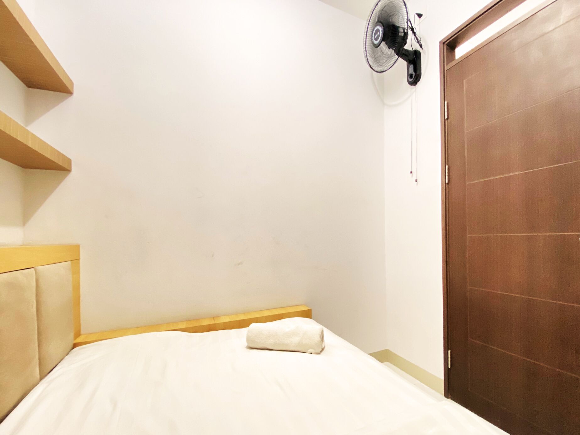 Ein Hotelzimmer mit Bett, Holz-Kopfteil, Wandventilator und Holzschrank.
