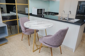 Une cuisine moderne avec un îlot en marbre blanc, deux chaises violettes, un four à micro-ondes et une cuisinière à gaz.