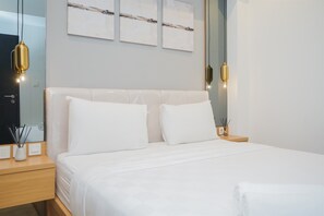Ein ordentlich bezogenes Bett mit weißen Leinen, ein Nachttisch aus Holz mit einer kleinen Vase und Kerzen, und eine Wand mit drei abstrakten Bildern.