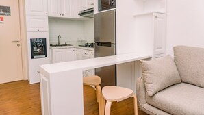 A compact kitchen with white cabinets, a stainless steel refrigerator, a microwave, and a small stool. - Fancy 2Br Apartment At M-Town Residence Near Summarecon Mall (Gading Serpong)