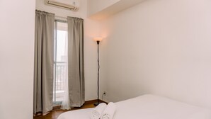 A hotel room with a bed, a standing floor lamp, and a window with curtains. - Fancy 2Br Apartment At M-Town Residence Near Summarecon Mall (Gading Serpong)