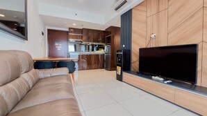 A modern living room with a leather sofa, a flat-screen TV, and a kitchen area in the background. - Great Deal And Cozy 2Br At M-Town Signature Apartment (Gading Serpong)