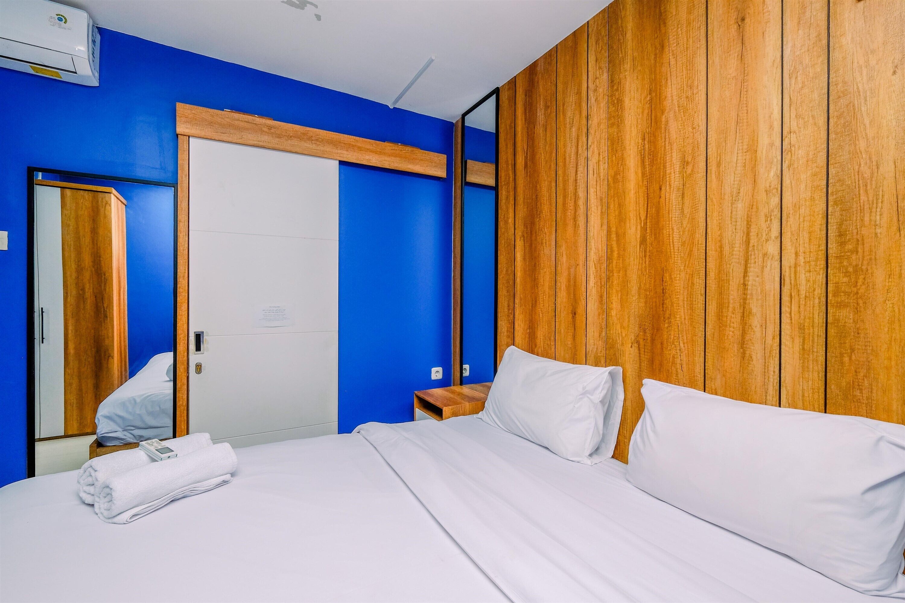 A hotel room with a bed, a wooden headboard, a blue wall, and a white door.