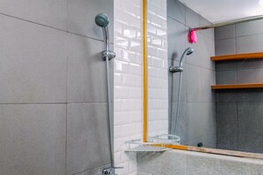 Une salle de bain avec des murs recouverts de carreaux gris, un espace de douche également carrelé de blanc, une étagère en bois et un miroir.