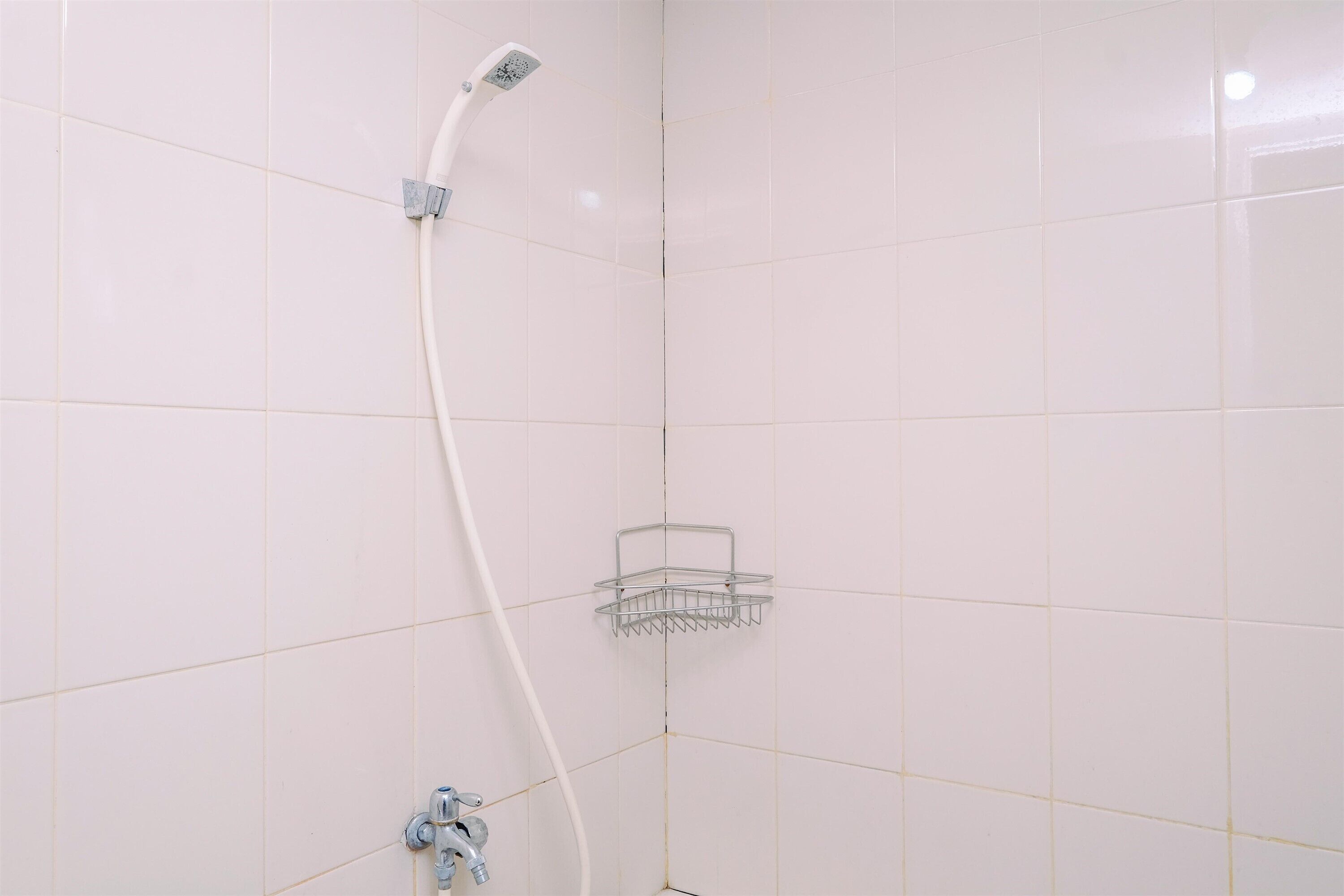 A corner of a bathroom with white tiled walls, a showerhead, and a metal shower caddy.