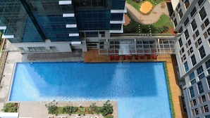 A modern building with a rooftop swimming pool, surrounded by greenery and a landscaped area. - Elegant And Comfy Studio At Tamansari Iswara Apartment (Bekasi)