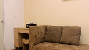 A room with a brown sofa, a wooden desk, and a closed door. - Cozy Studio At Metropark Condominium Jabebeka Apartment (Cikarang)
