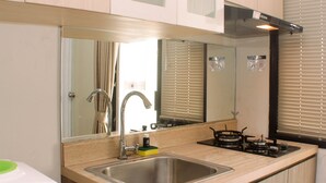 A modern kitchen with a stainless steel sink, a gas stove, and a large mirror above the countertop. - Cozy Studio At Metropark Condominium Jabebeka Apartment (Cikarang)
